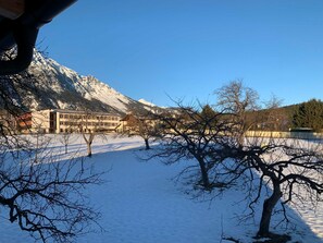 Schneebedeckte Landschaft mit einem Gebäude mit mehreren Fenstern und einem Berg im Hintergrund.