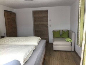 Ein Schlafzimmer mit einem Bett, einem kleinen Sofa, einer Holztür und einem Lichtschalter an der Wand.