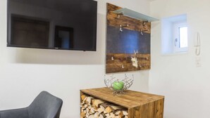 A living room with a flat-screen TV, a wooden wall art piece, a green decorative bowl, and a stack of firewood. - Apartment Boskop - Schusterbrand Apartments (Absam)