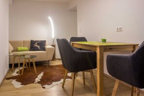 Ein Essbereich mit Holztisch, schwarzen Stühlen, einem Tisch mit Glasplatte, einem Kuhfellteppich und einer Couch mit grünem Kissen.