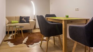 A dining area with a wooden table, black chairs, a glass-top table, a cowhide rug, and a sofa with a green pillow. - Apartment Boskop - Schusterbrand Apartments (Absam)