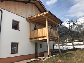 A two-story building with a wooden balcony, white walls, and a mountain backdrop. - Boskop Apartment - Schusterbrand Apartments (Absam)