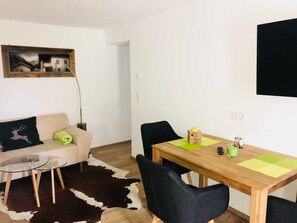 Un salon comprenant un canapé, une table basse en verre, une table à manger avec des chaises, un tapis en peau de vache, un tableau et un téléviseur fixé au mur.