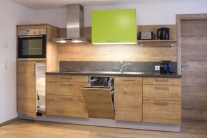 A modern kitchen with wooden cabinets, a built-in oven, a dishwasher, a stainless steel sink, and a green cabinet above the countertop.