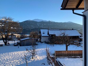 A snowy landscape with houses, a wooden fence, and mountains in the background. - Jonagold Apartment - Schusterbrand Apartments (Absam)