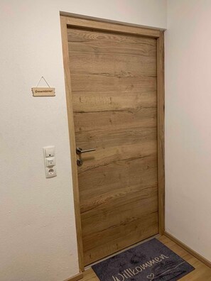 A wooden door with a handle, a small sign above it, and a doormat at the entrance. - Gravensteiner - Schusterbrand Apartments (Absam)