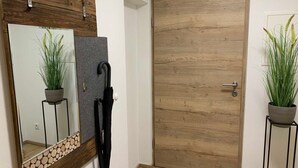 A hallway with a wooden door, a mirror with a plant, and a black umbrella. - Gravensteiner - Schusterbrand Apartments (Absam)
