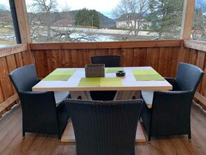 A wooden deck with a table and chairs, a wicker chair, and a view of a snowy landscape. - Gravensteiner - Schusterbrand Apartments (Absam)