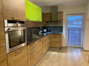 A modern kitchen with wooden cabinets, a stainless steel oven, a sink, and a window with a view. - Gravensteiner - Schusterbrand Apartments (Absam)