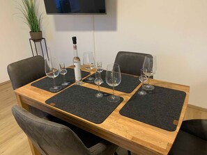 A dining table with four chairs, a bottle of wine, and several empty wine glasses. - Gravensteiner - Schusterbrand Apartments (Absam)