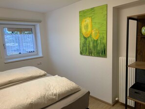 Une chambre à coucher avec un lit, une fenêtre, un radiateur et un tableau accroché au mur.