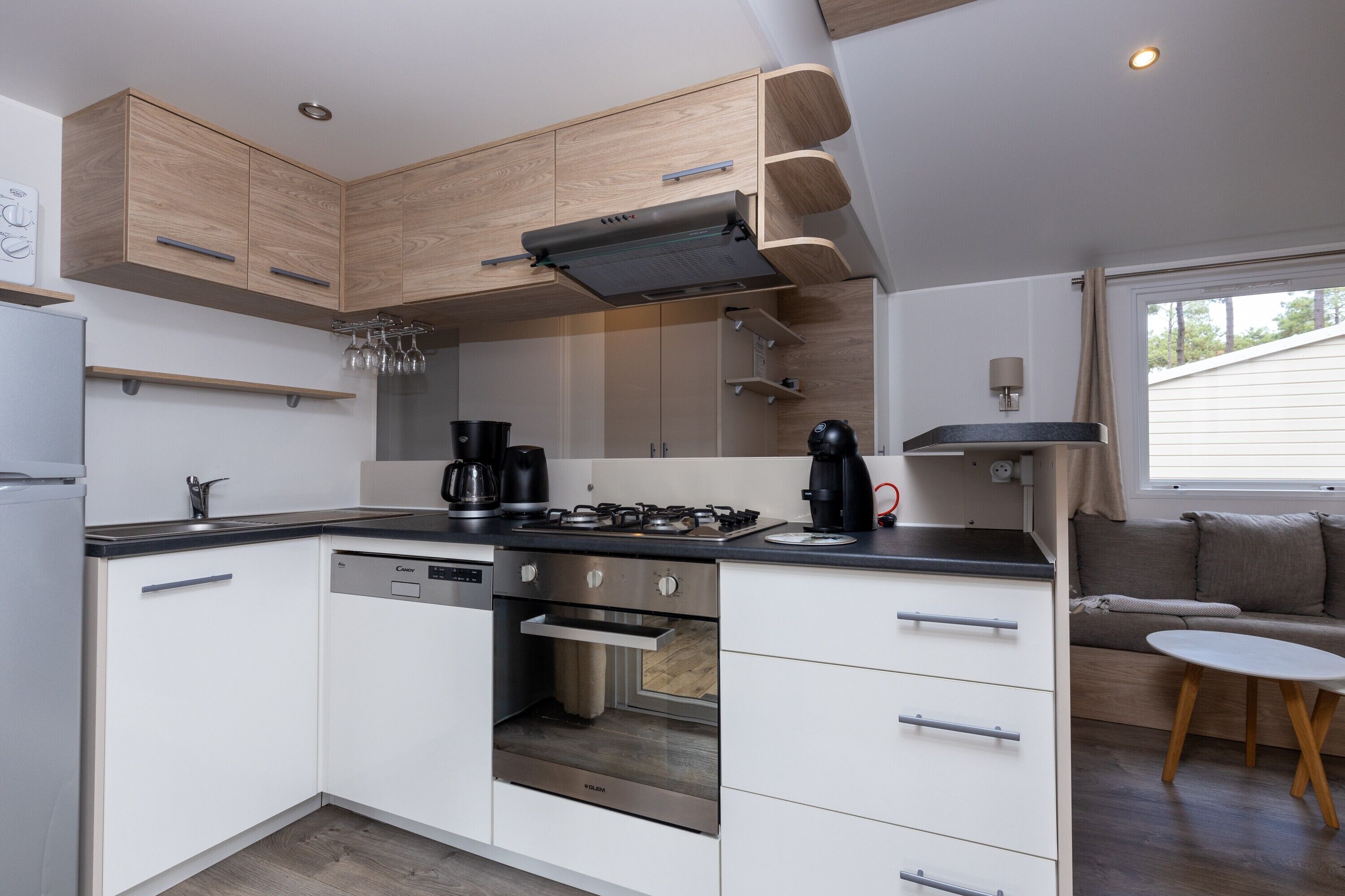 A compact kitchen with built-in appliances, wooden cabinets, and a dining area with a table and bench.