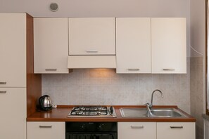 Une cuisine avec des meubles blancs, une cuisinière à gaz, un évier et une bouilloire.