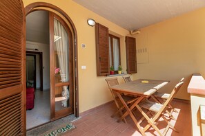 Une pièce avec une table et des chaises en bois, une porte portant un numéro et une fenêtre avec des volets.