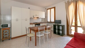 Une cuisine compacte avec des meubles blancs, une table à manger avec des chaises, un canapé rouge et un téléviseur posé sur un meuble.