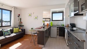 Ett modernt kök med en inbyggd diskmaskin, en matplats med soffa och stolar samt ett stort fönster som släpper in naturligt ljus.