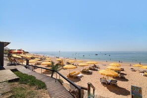 Une plage avec des parasols jaunes, des chaises longues et une terrasse en bois donnant sur la mer.