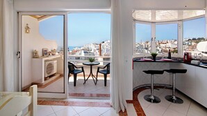 A modern apartment with a balcony, a kitchen with bar stools, and a view of the city. - Apartment Paradis Bleu with Sea View, Shared Pool, Wi-Fi & A/C (Albufeira)