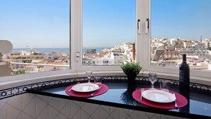 A dining area with a view of a coastal city, a potted plant, and a bottle of wine on the table. - Apartment Paradis Bleu with Sea View, Shared Pool, Wi-Fi & A/C (Albufeira)