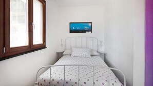 Quarto com cama, janela, televisão na parede e mesa de cabeceira.