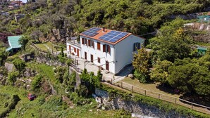 Um edifício branco com telhado de telhas vermelhas, painéis solares e uma parede de pedra.