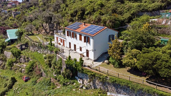 A white building with a red-tiled roof, solar panels, and a stone wall.