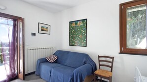 Quarto com sofá azul, uma cadeira de madeira, radiador, janela com vista e duas imagens emolduradas na parede.