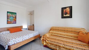 A bedroom with a bed, a sofa, a nightstand, and two framed pictures on the wall. - Apartment 'Fattorialmare Gialla' with Sea View, Shared Terrace & Wi-Fi (Camogli)