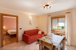 A room with a bed, a red sofa, a dining table with chairs, a window with curtains, and a ceiling fan.