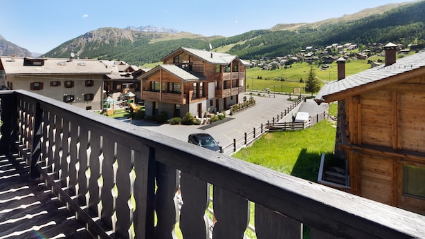 Un edificio in legno con un balcone, un'auto parcheggiata di fronte e un paesaggio montuoso sullo sfondo.