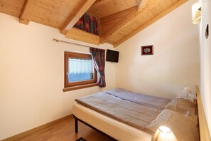Une chambre à coucher avec un lit, une fenêtre avec des rideaux, un téléviseur fixé au mur et un petit tableau encadré accroché au mur.