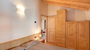 Un dormitorio con cama, armario de madera y lámpara fijada a la pared.