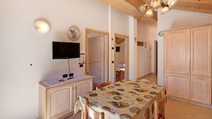 Comedor con mesa, sillas, televisor, armarios de madera y lámpara en el techo.