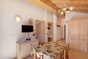 Comedor con mesa, sillas, televisor, armarios de madera y lámpara en el techo.