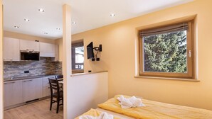 Une chambre avec deux lits, un coin cuisine et une fenêtre donnant sur les arbres.