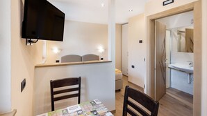 Une chambre d’hôtel moderne dotée d’un téléviseur à écran plat fixé au mur, d’un coin repas avec une table et des chaises, et d’une salle de bain séparée avec un lavabo et un miroir.