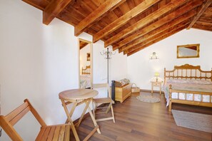 Ein Schlafzimmer mit Holzbalkendecke, einem Bett mit gemustertem Überwurf, einem Nachttisch mit Lampe, einem Holzstuhl und einem kleinen Rundteppich.