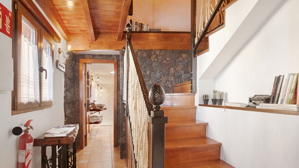 Una escalera de madera con un muro de piedra, un extintor y una pequeña mesa con papeles.