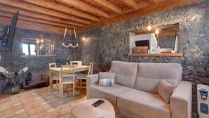 Una habitación acogedora con pared de piedra, vigas de madera en el techo, un sofá, una mesa de comedor y sillas.