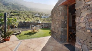 Un espacio al aire libre con paredes de piedra, un patio, sillas y un pequeño césped.