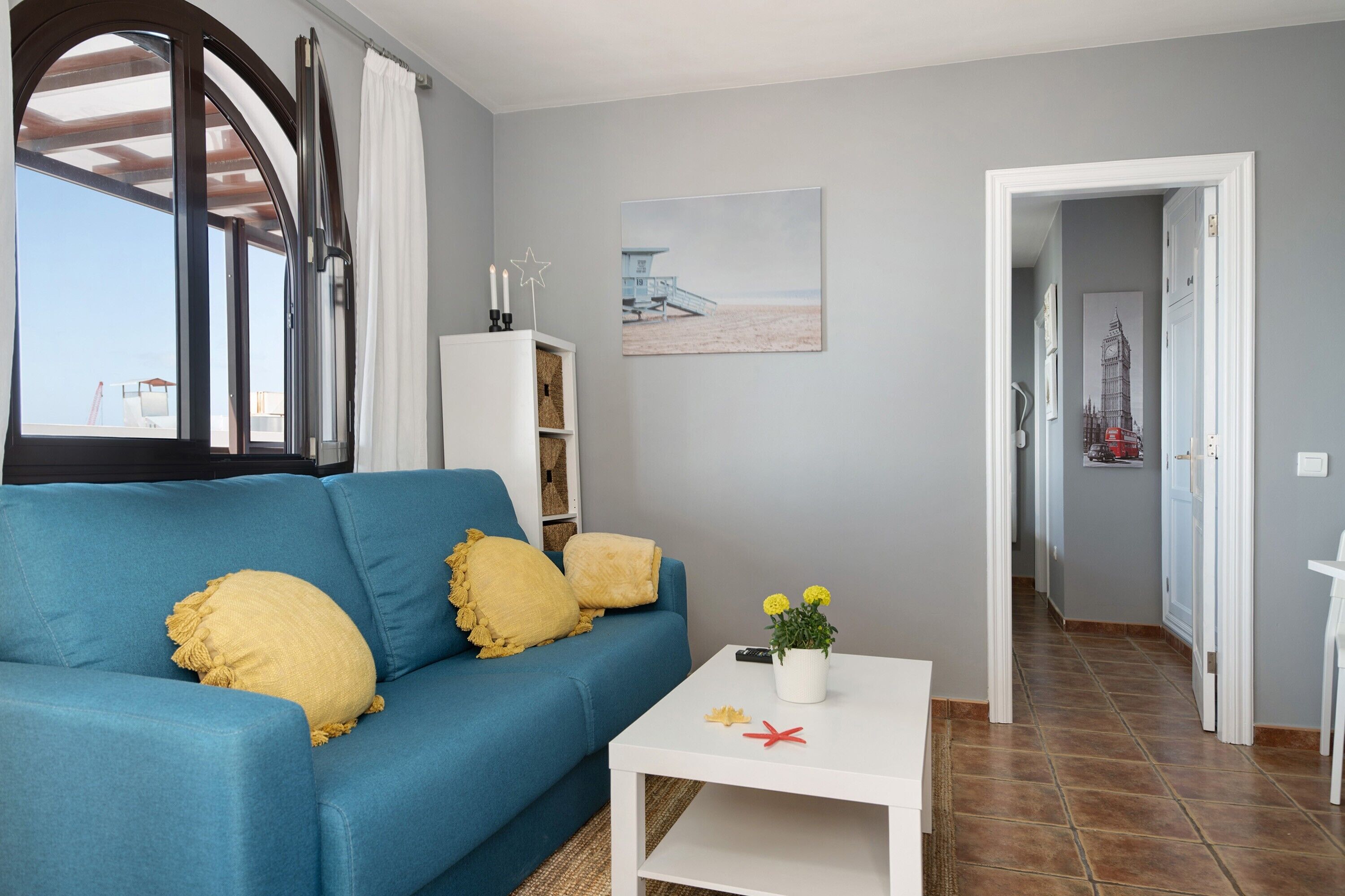 Een woonkamer met een blauwe bank, een witte salontafel en een schilderij aan de muur.
