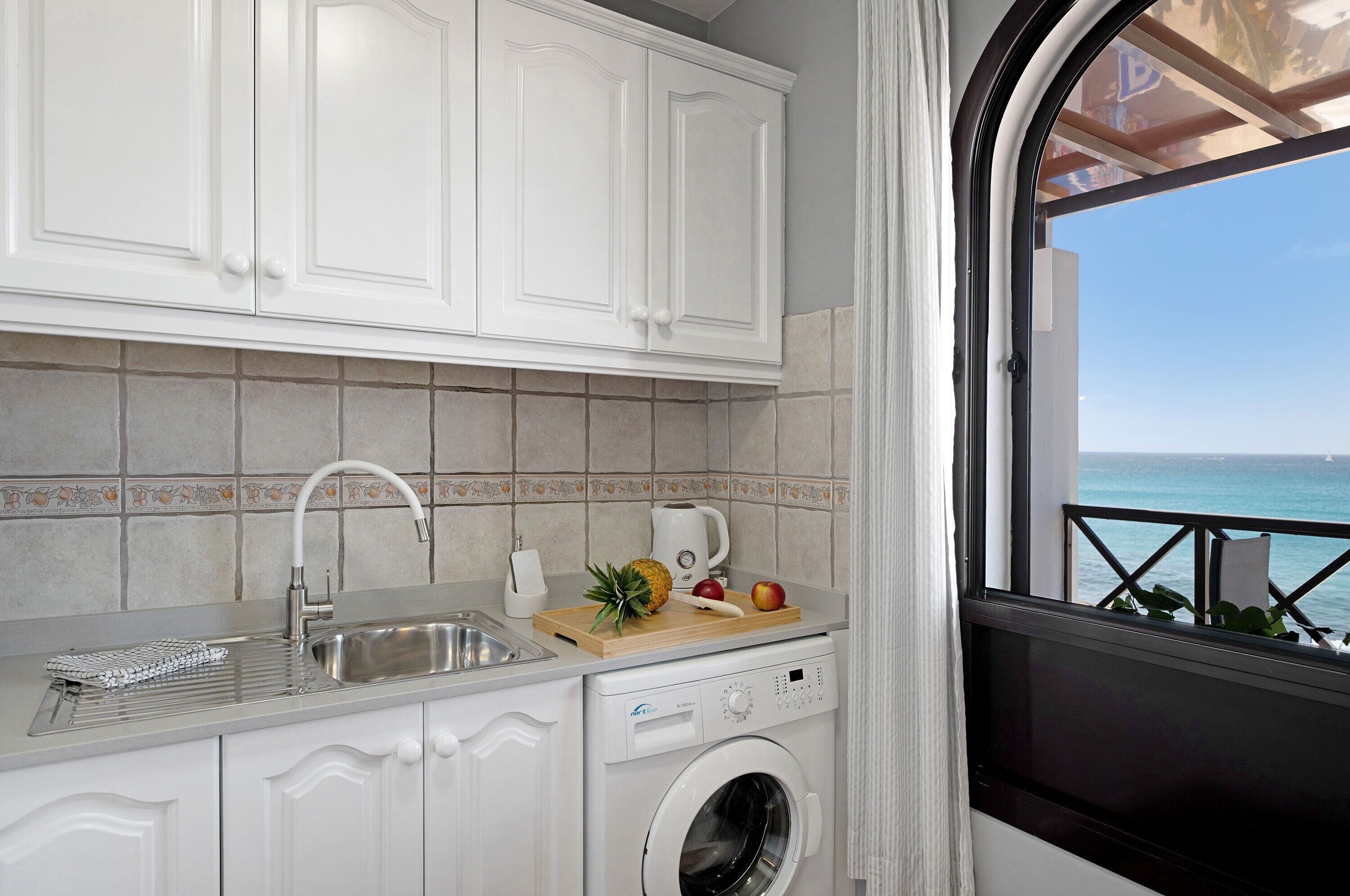 Una cocina compacta con lavadora, un lavamanos y ventana con vistas al mar.