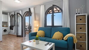En stue med sofa, sofabord, lampe og udsigt til himlen gennem store vinduer.