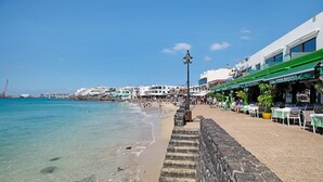 En kystpromenade med stenvæg, strand og bygninger ved havet.