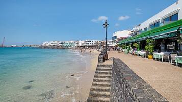 Un paseo marítimo con muro de piedra, playa y edificios frente al mar.