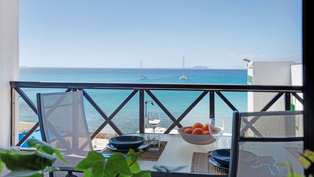 En balkon med et spisebord, der ud til et klart, blå hav med både.