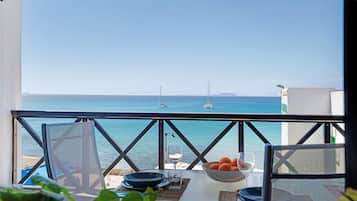 Un balcón con mesa dispuesta para comer, con vista a un mar azul y despejado con barcos.