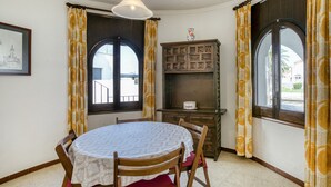 Un comedor con una mesa redonda, sillas, un aparador y dos ventanas con cortinas.
