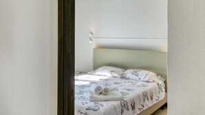 Una cama con una colcha estampada, una toalla enrollada y un aire acondicionado instalado en la pared.