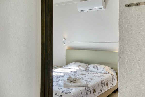 Un lit recouvert d’une couvre-lit à motifs, une serviette enroulée et un climatiseur fixé au mur.